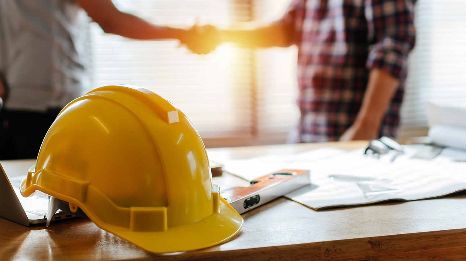 Two Business Men Shaking Hands with a Yellow Construction Hard Hat in the Foreground